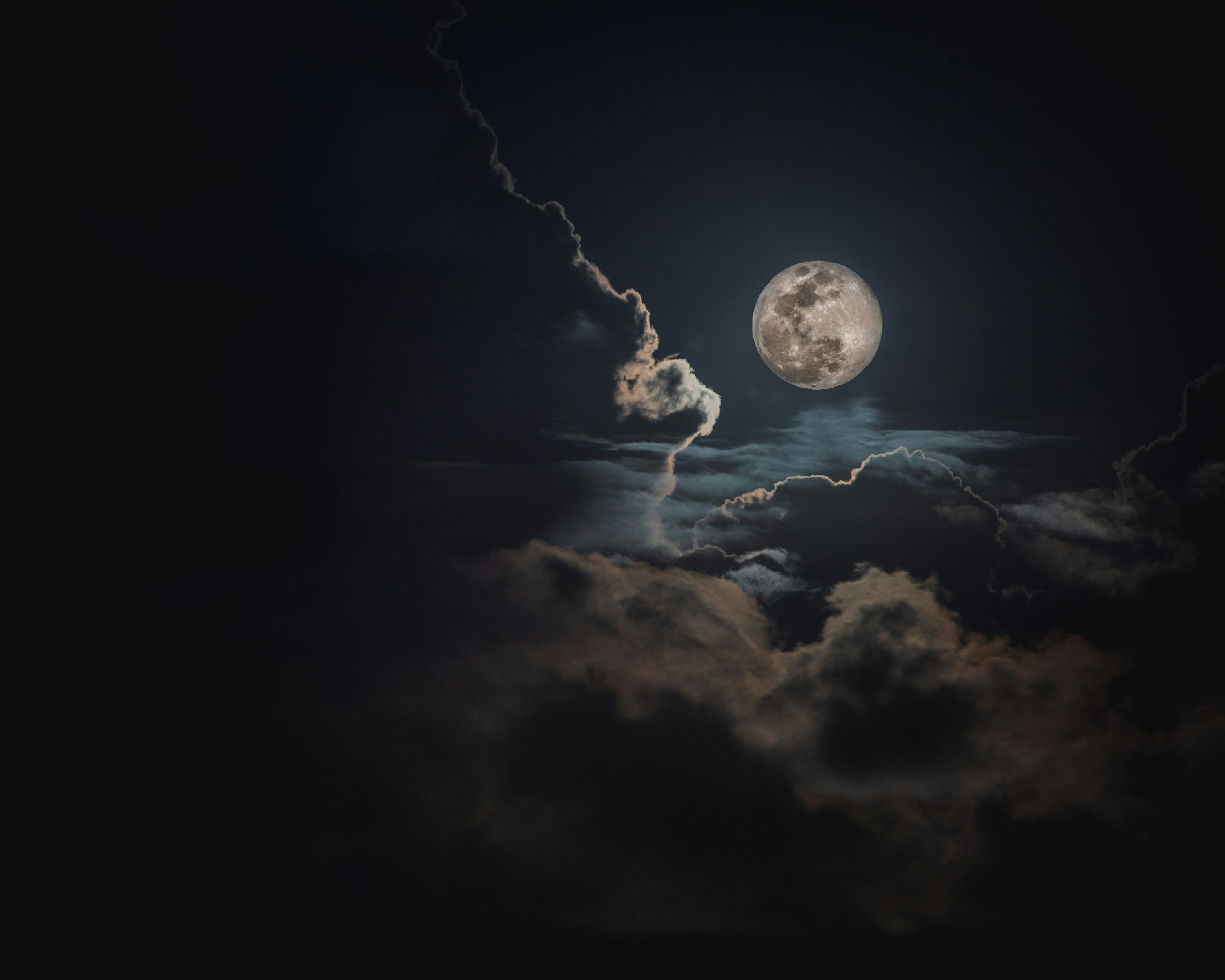 Full moon glowing between dark clouds