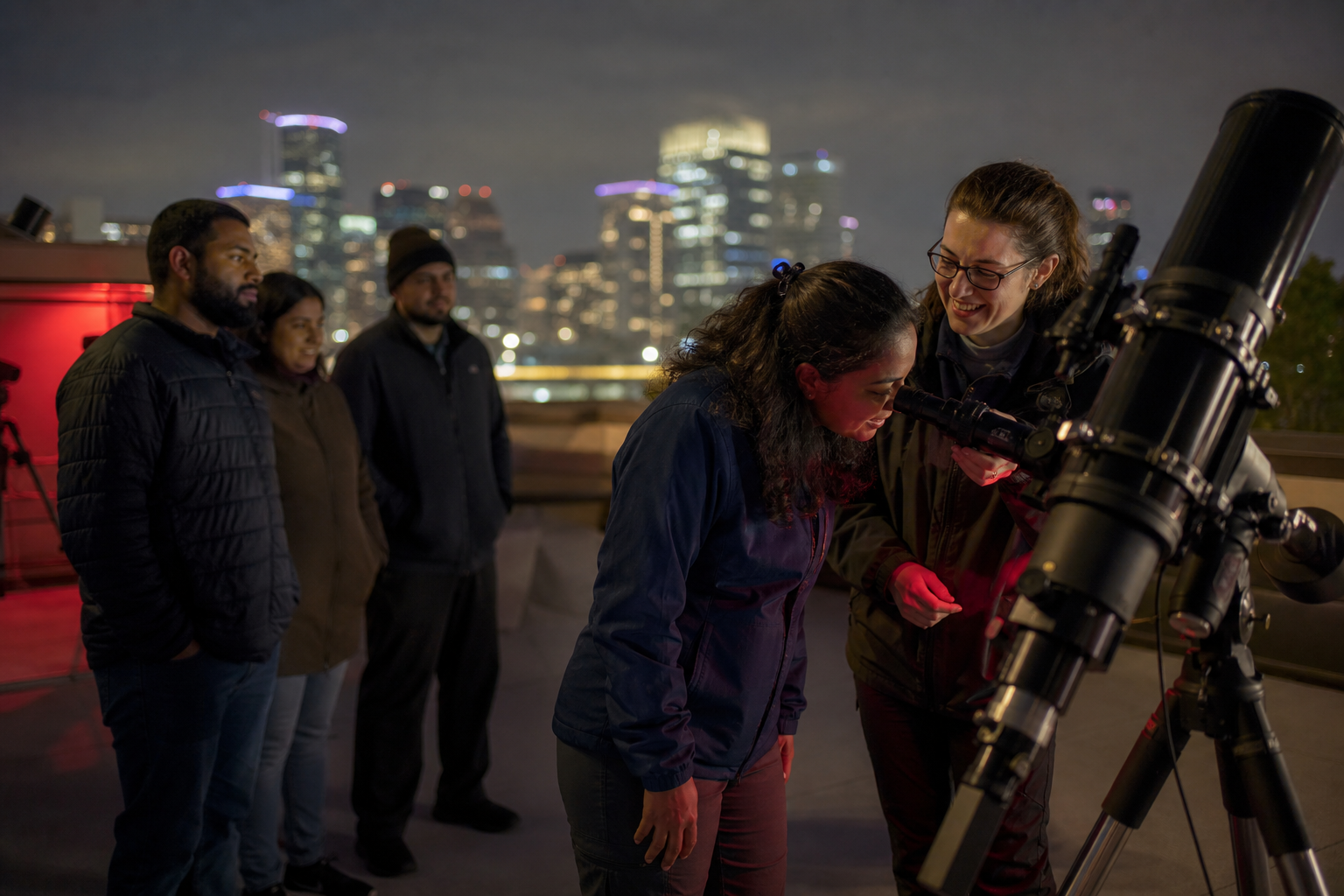 An astronomer helps a beginner view an object through a rooftop telescope