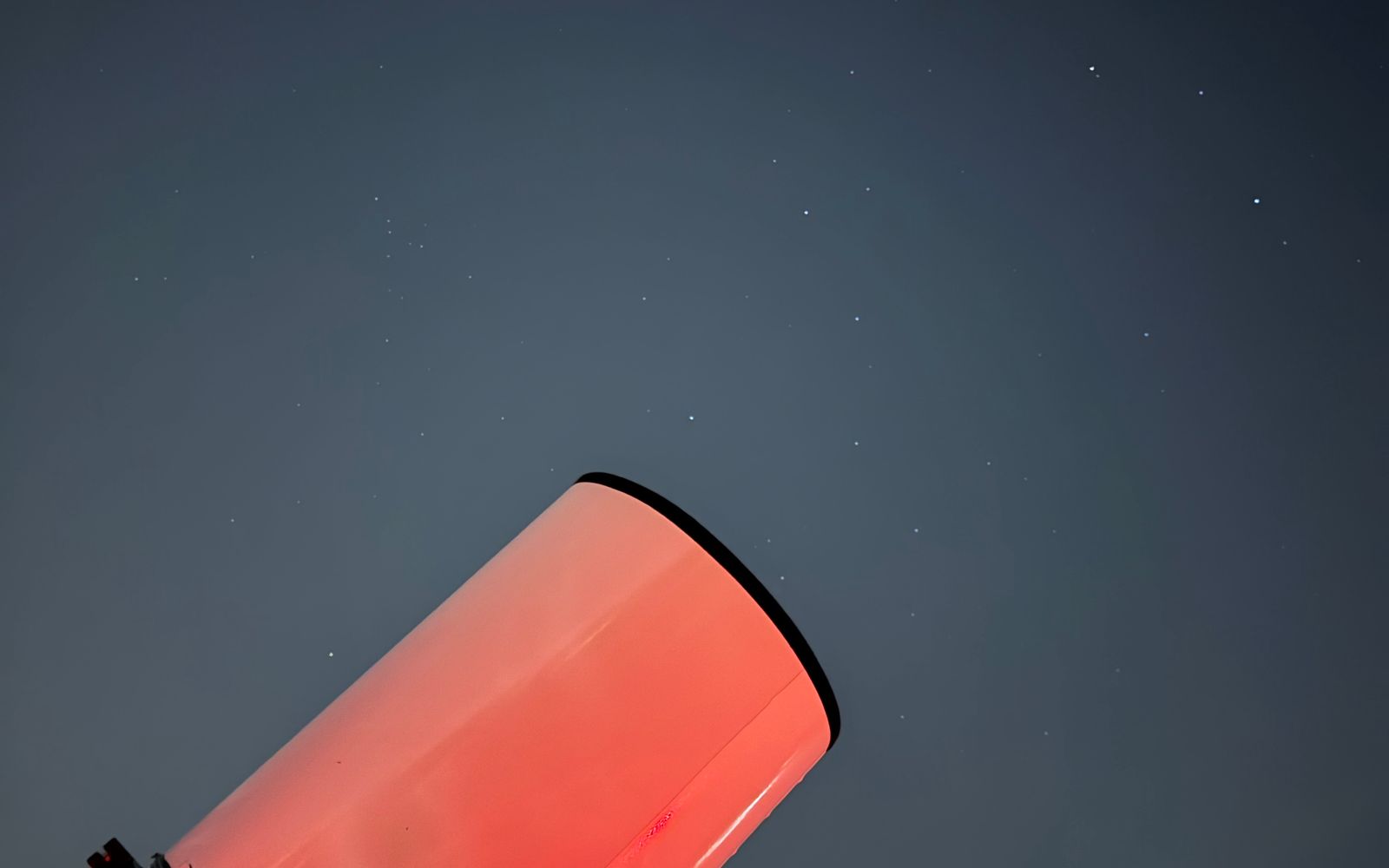 Telescope illuminated by a dim red observing light beneath a starry night sky
