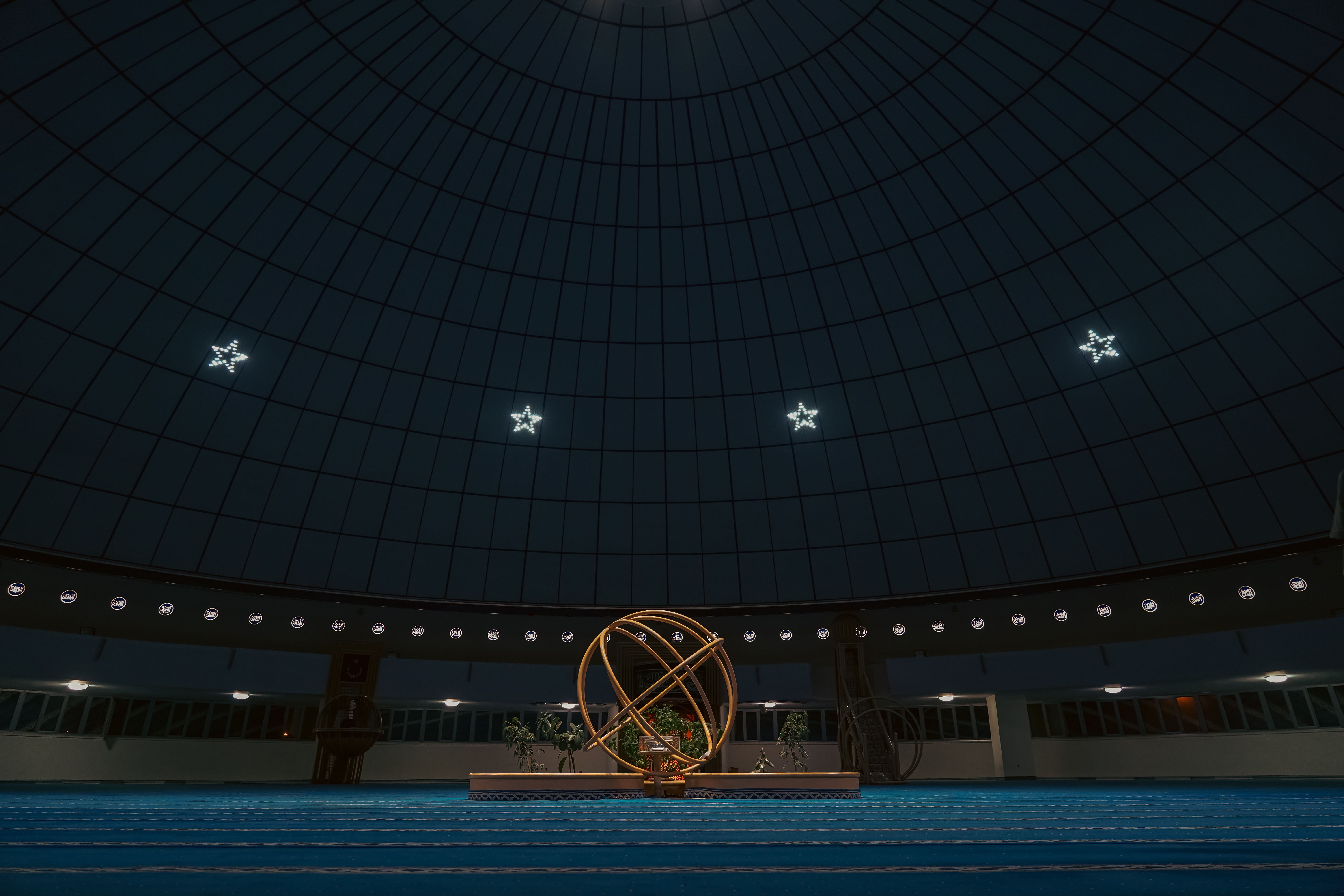 A modern planetarium interior with a starry dome and central astronomical sculpture.