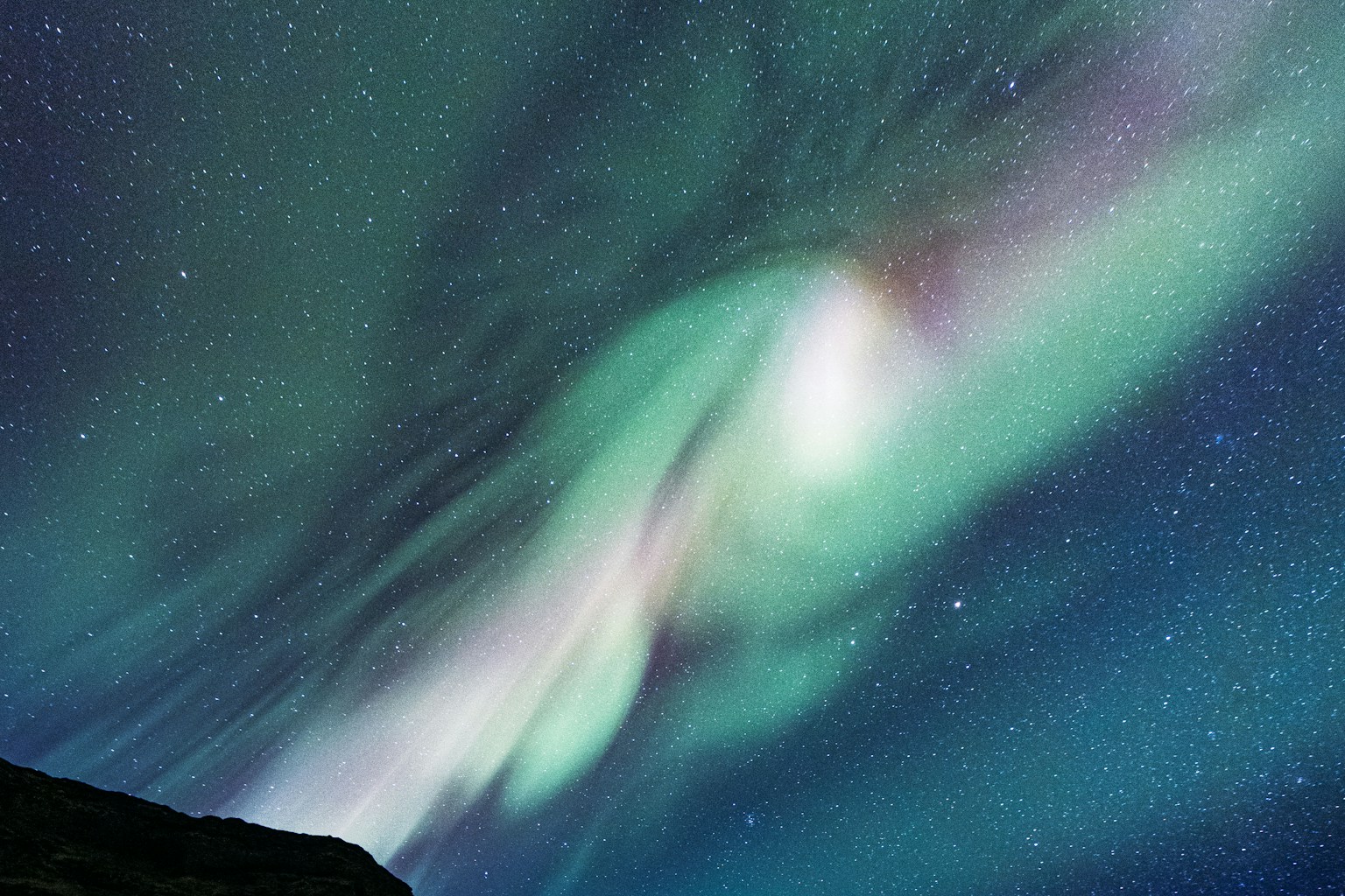 Green aurora above dark ocean cliffs and a starry night sky