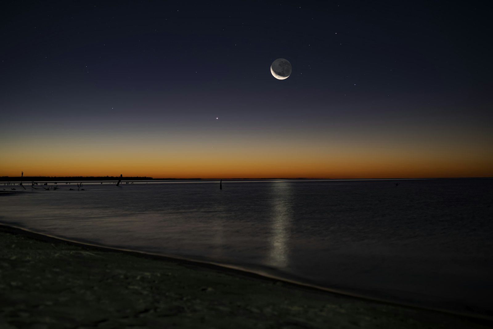 Crescent moon and stars above a calm ocean horizon at dusk