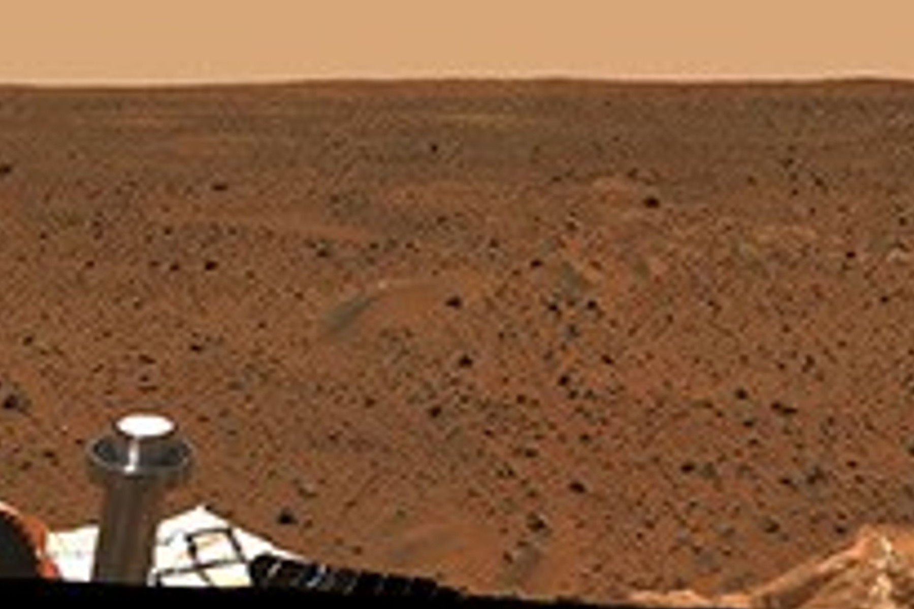 Panoramic Mars surface photographed by NASA’s Spirit rover, showing a rocky horizon beneath a pale sky.