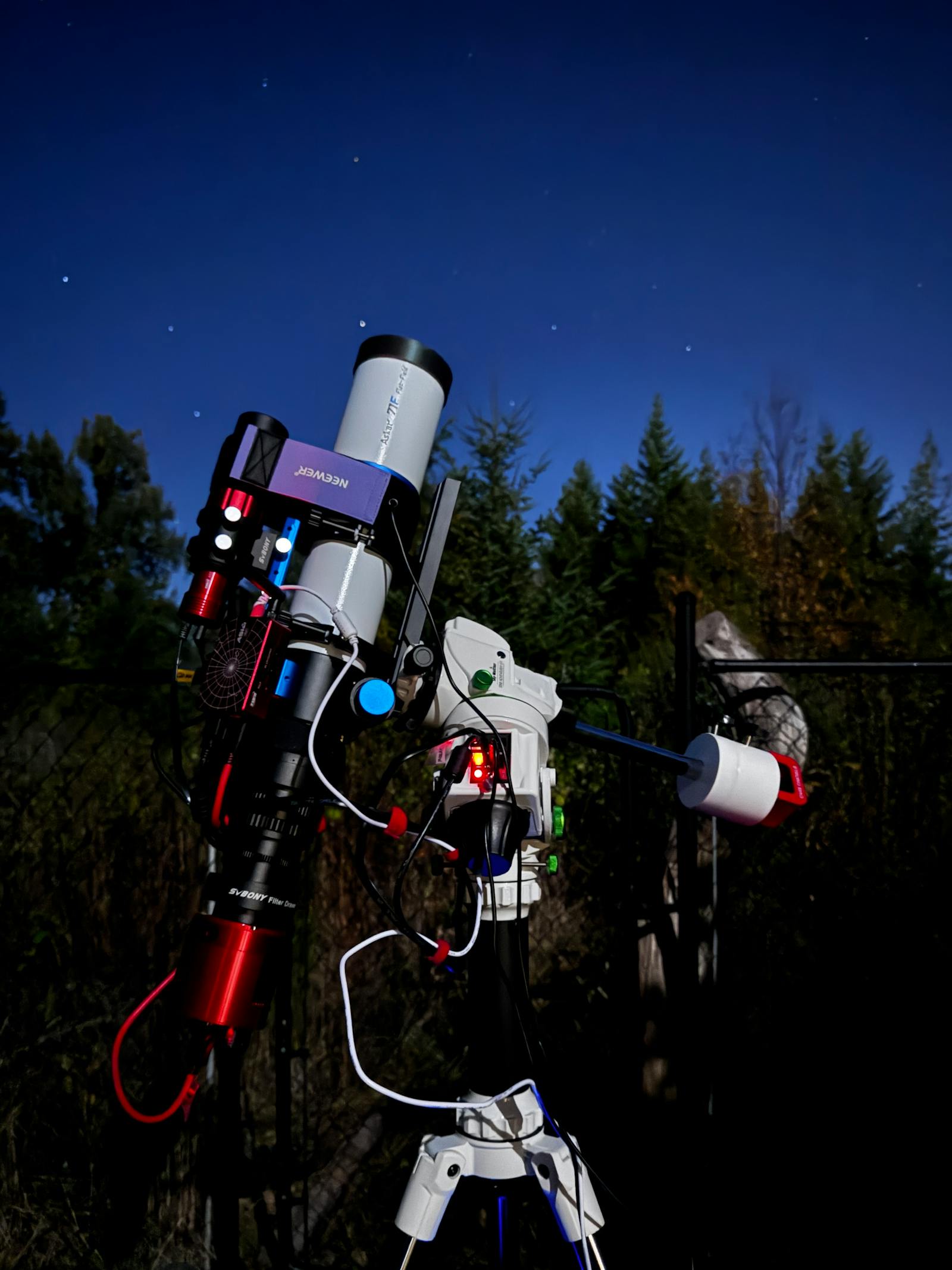 White refractor telescope on an equatorial mount aimed at a twilight sky