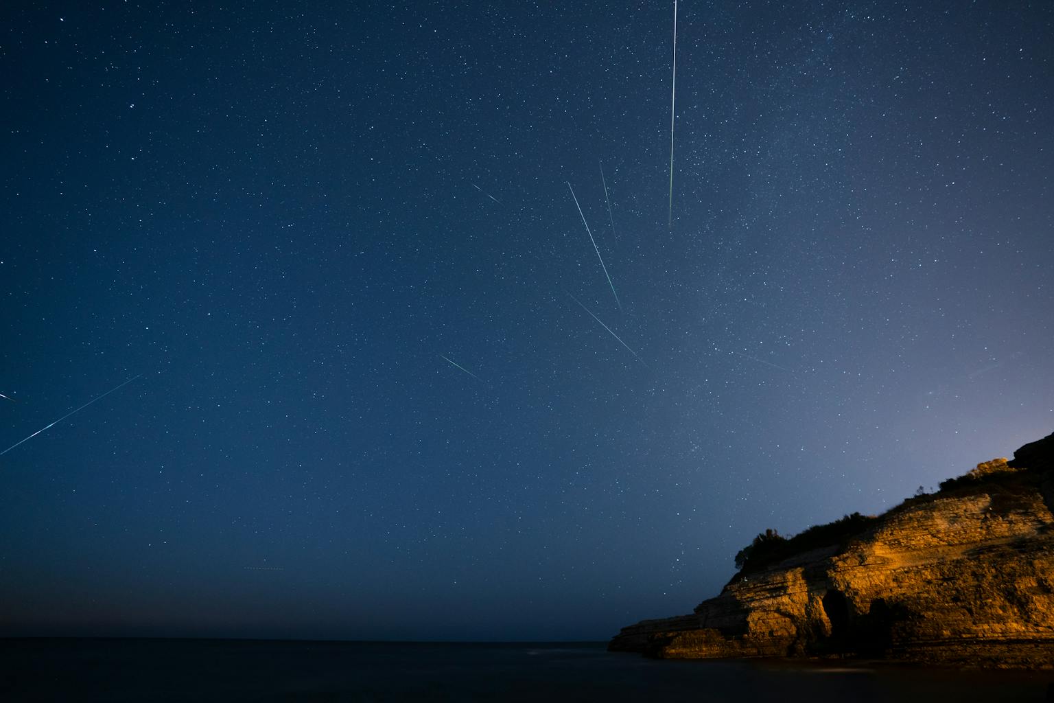 Meteor streaks over moonlit rocky cliff