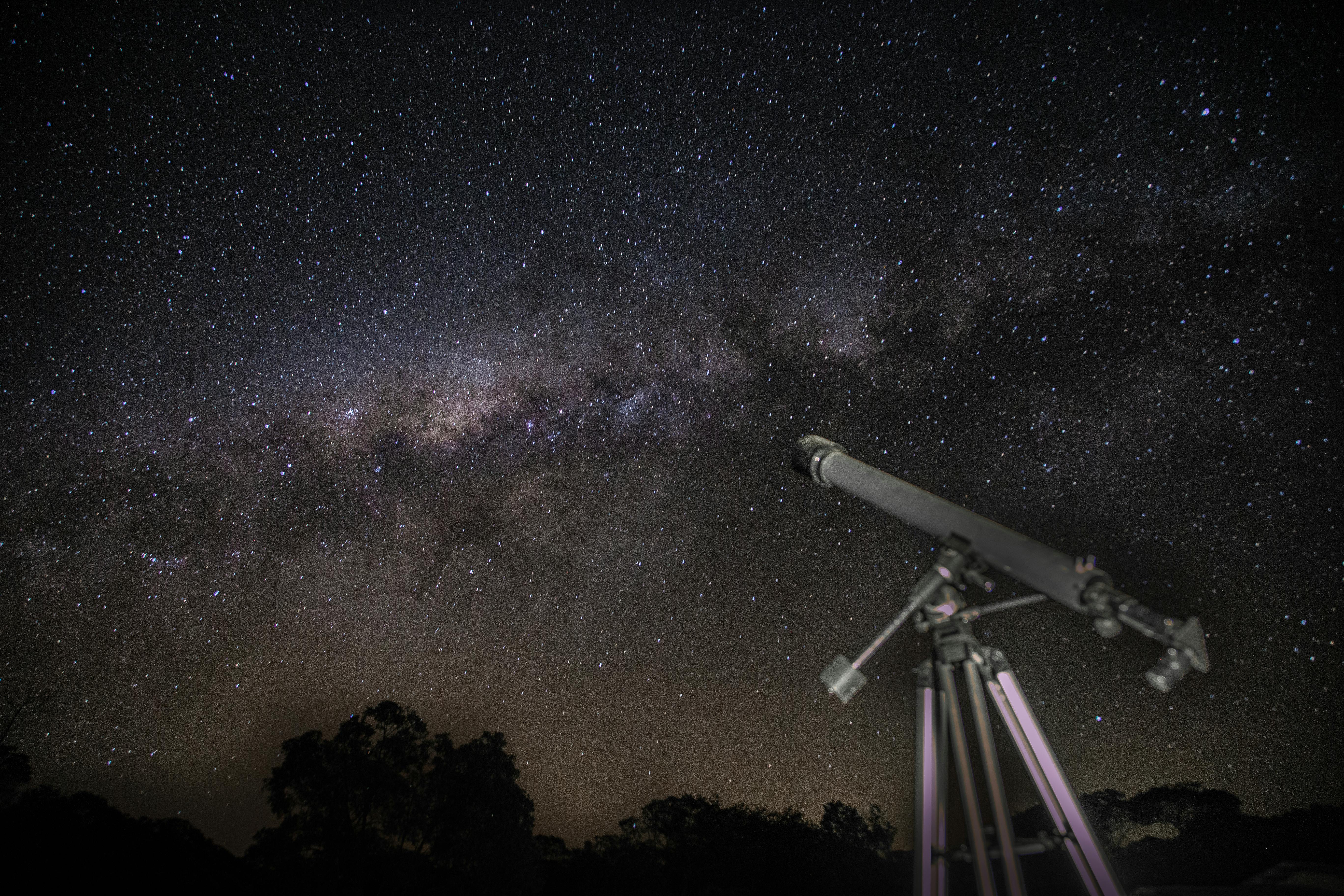 Classic telescope aimed toward the Milky Way over a dark horizon
