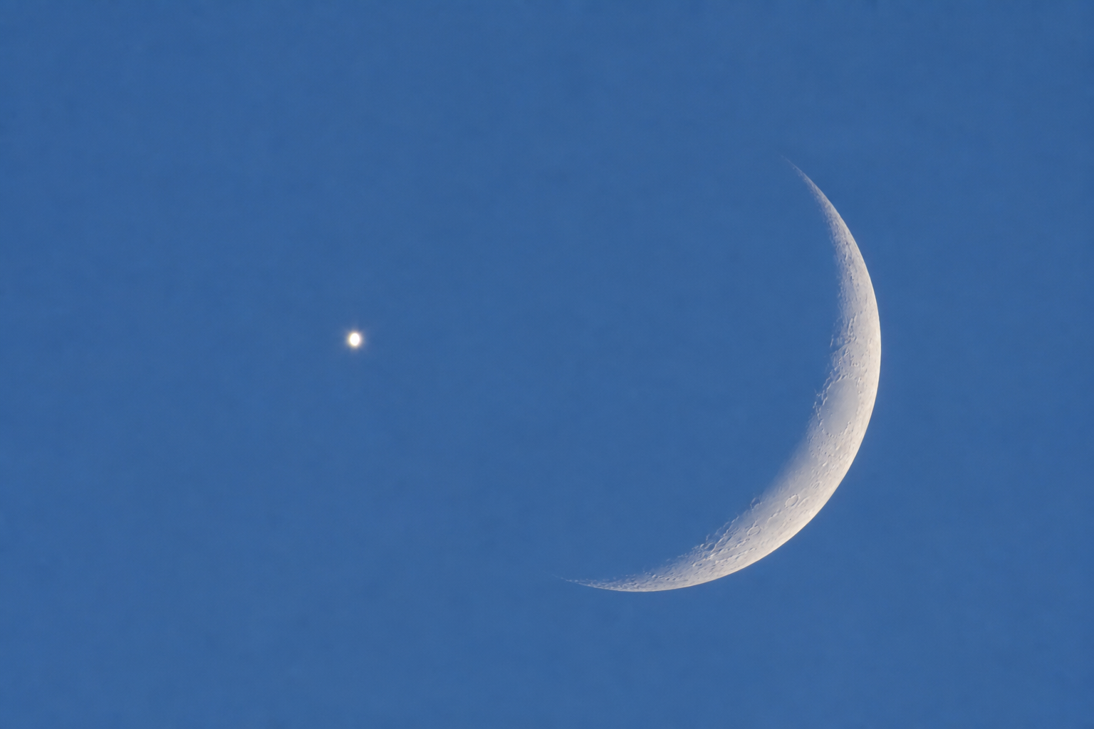 Close telescopic-style view of Venus near the thin crescent Moon in a blue daytime sky