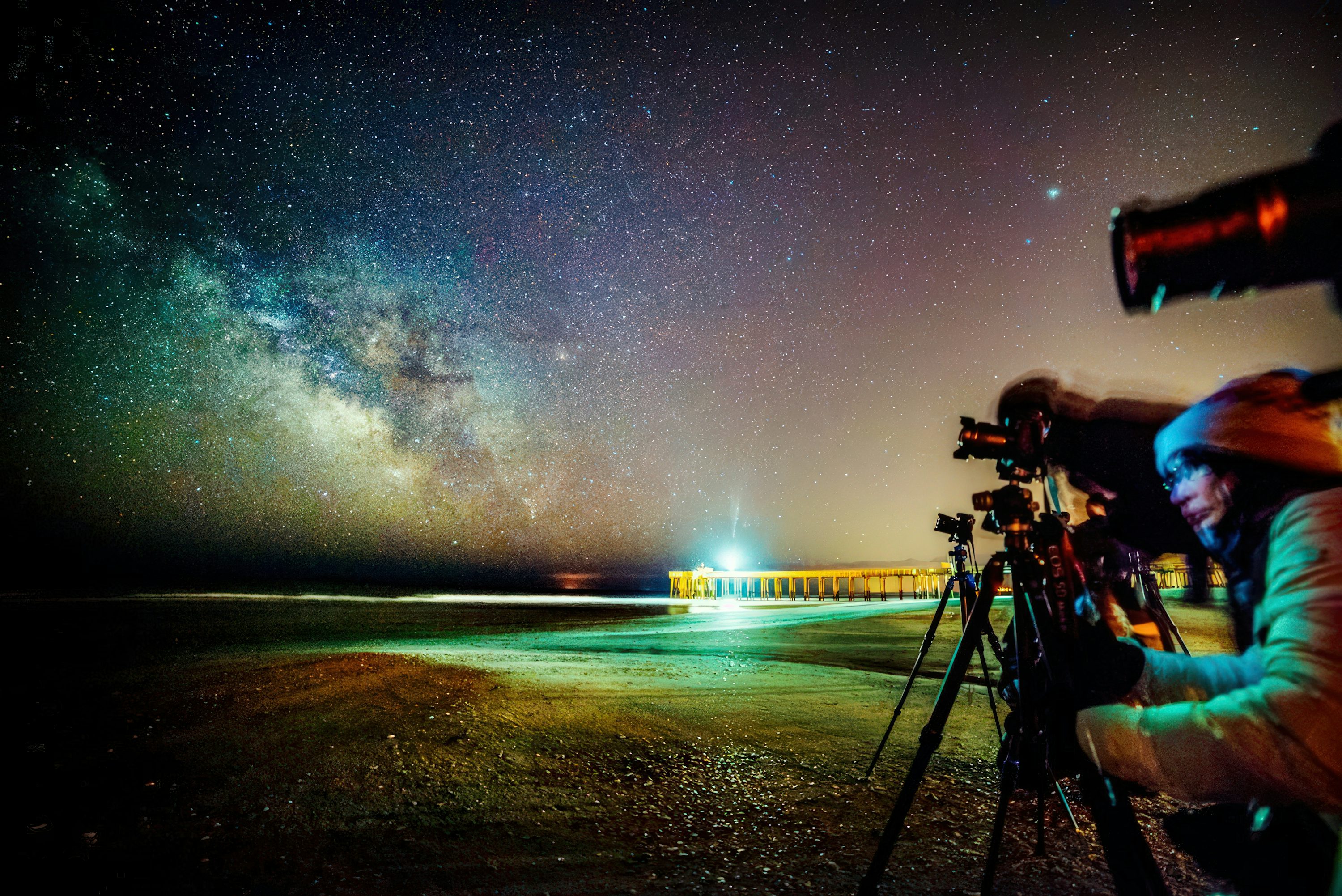 Group of astrophotographers with telescopes and tripods on a beach beneath the Milky Way