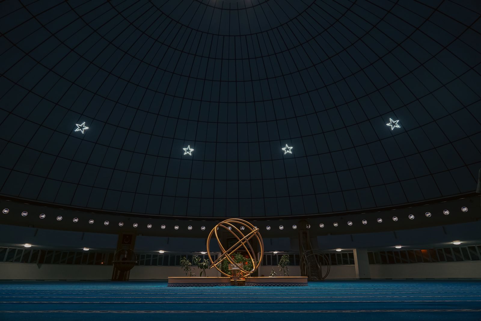 Dark planetarium dome with a central astronomical sculpture and star-shaped lights.