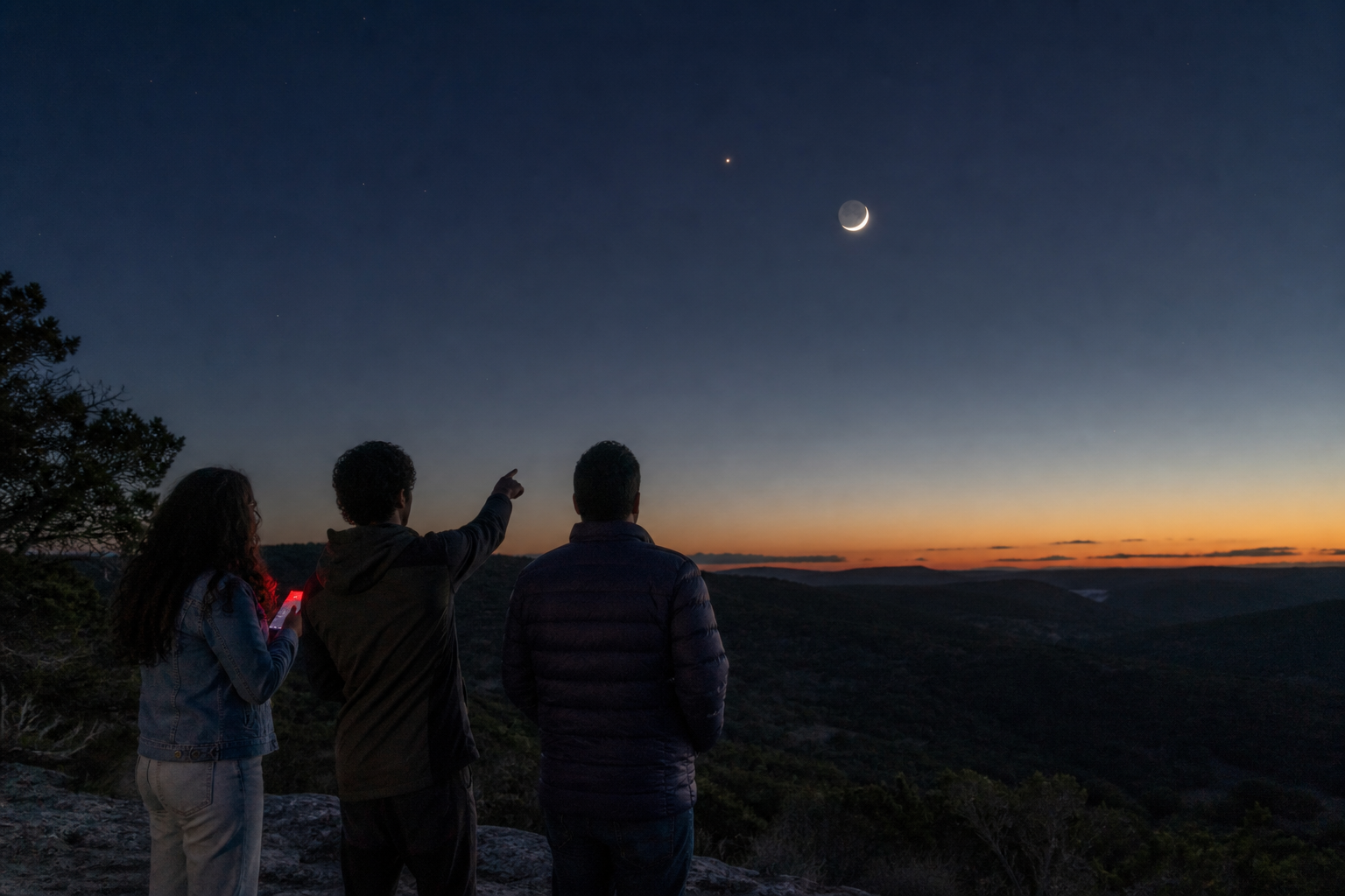 Three friends use a dim red phone screen while sharing a pre-dawn skywatch from a Hill Country overlook.