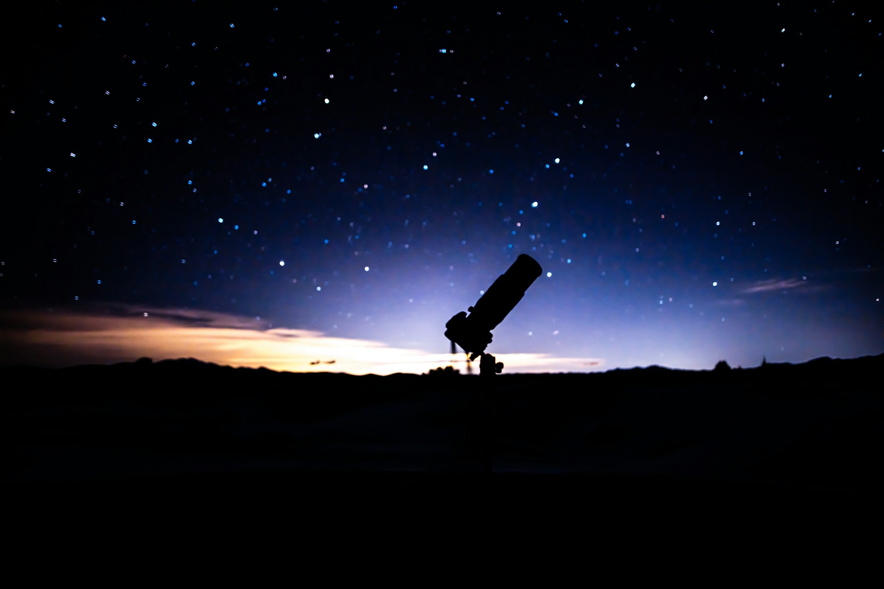 A telescope on a hill beneath a deep-blue night sky.
