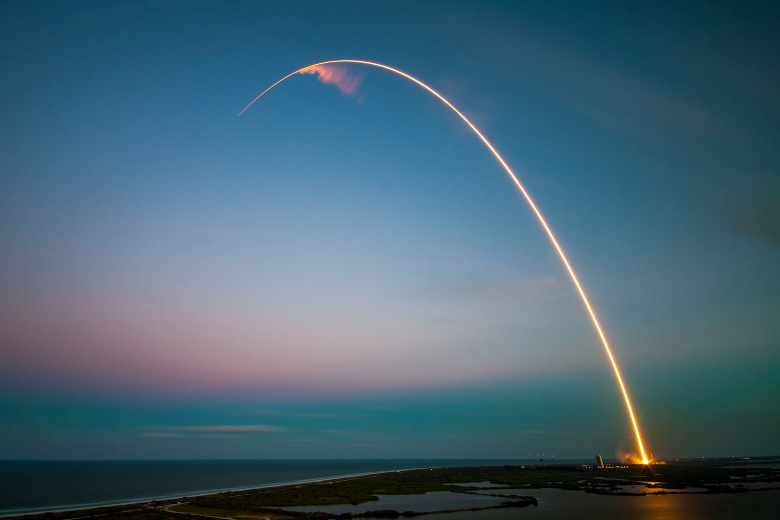 Long-exposure rocket launch arc above dark coastal water at dusk, representing BOHR's ride to orbit on SpaceX Transporter-17