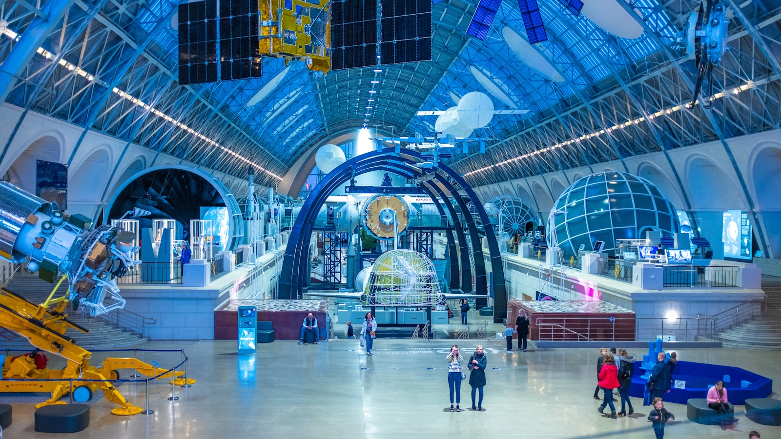 Visitors explore a blue-lit space museum gallery with spacecraft exhibits